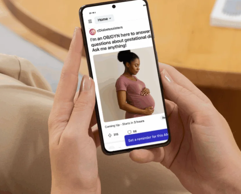 A person holds a smartphone displaying a social media post of a pregnant woman in a pink shirt cradling her belly, featuring text about an upcoming Reddit AMA on gestational diabetes with an OB/GYN answering questions.