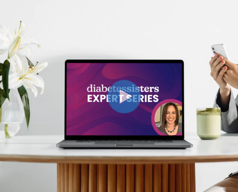 A person sits at a round table holding a phone, with a laptop displaying the “DiabetesSisters Expert Series” focused on the value of peer support and diabetes education. White flowers in a vase sit beside the laptop.