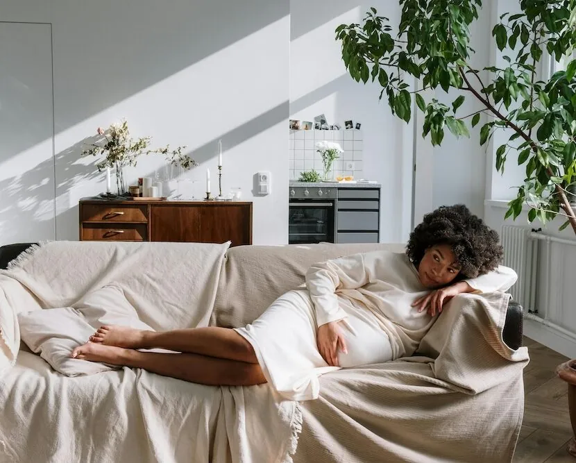 Pregnant woman resting on a sofa at home, gently holding her belly.