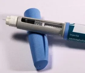 A close-up of a semaglutide injection pen with a visible needle, placed on a white surface next to its blue protective cap.