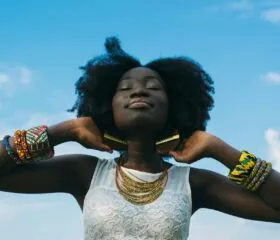 A woman with natural hair and colorful jewelry stands confidently with her eyes closed under a blue sky, embodying strength and resilience in her Type 1 diabetes journey.