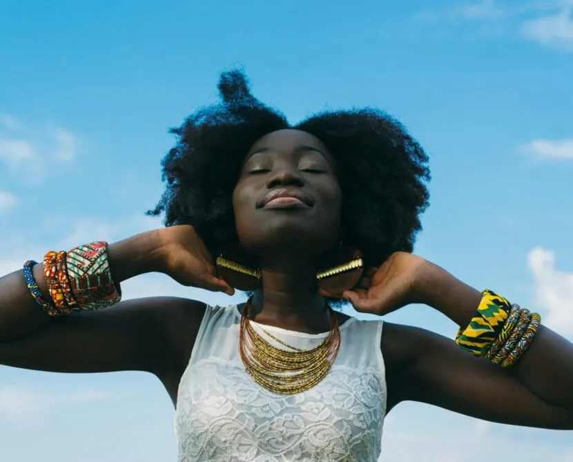 A woman with natural hair and colorful jewelry stands confidently with her eyes closed under a blue sky, embodying strength and resilience in her Type 1 diabetes journey.